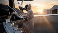 Elegant senior woman in beige coat boarding private jet at sunset, luxury travel and lifestyle concept for affluent mature travelers.