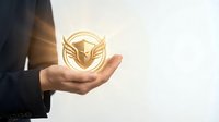 Golden shield with wings icon glowing in open palm of businessperson, symbolizing protection, security, and trust for corporate branding and business concepts.