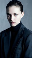 Professional young Caucasian businesswoman in dark suit with slicked back hair and intense blue eyes against gray background for corporate branding.