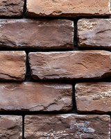 Rough textured brown brick wall with uneven surfaces and dark mortar joints creates rustic architectural background pattern for design and construction projects.