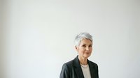 Mature woman with short gray hair wearing dark blazer and cream top, isolated on white background for corporate, business, and professional portrait use.