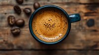 Fresh brewed espresso with golden crema in dark blue ceramic cup on rustic wooden background with scattered coffee beans, top view composition.