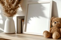 Minimalist home decor mockup with white frame, ceramic vase with pampas grass, books and brown teddy bear on wooden shelf in soft natural sunlight.