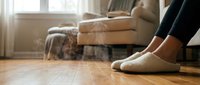 Cozy home atmosphere with female feet in soft slippers on warm wooden floor, steam rising, blurred living room background.
