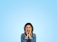 Young woman with dark curly hair and olive complexion expressing surprise and excitement with hands near face against blue background for advertising and marketing campaigns.