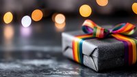 Gift box wrapped in black paper with rainbow pride ribbon on dark surface with blurred bokeh lights creating festive holiday atmosphere.