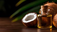 Coconut oil in glass bottle with fresh tropical coconuts on dark wooden background, natural organic cosmetic and cooking ingredient.