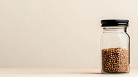 Glass jar filled with dried coriander seeds on beige background, minimalist food photography composition showing organic spice storage and preservation.