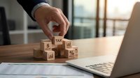 Business professional arranging wooden tax cubes on desk with laptop and financial documents for accounting and tax planning consultation services.