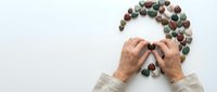 Elderly hands arranging colorful stones in question mark shape on white background symbolizing confusion, dementia, memory loss, aging concerns.