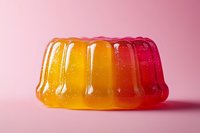 Colorful layered jelly dessert with orange and red gradient effect on pink background, showing translucent texture and rippled surface with glossy shine.