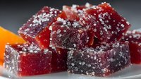 Red fruit gummy candy squares covered with sugar crystals on white plate, sweet confectionery treats for dessert and snacking occasions.