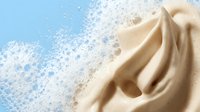 Creamy beige fabric swirls with white powder explosion on blue background for cosmetic beauty product advertising and skincare marketing materials.