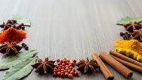Aromatic spices and herbs arranged on wooden surface including star anise, cinnamon sticks, turmeric, paprika, bay leaves and peppercorns for cooking.