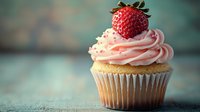 Fresh strawberry cupcake with pink swirled frosting and whole berry on top against rustic turquoise background, soft focus food photography styling.