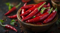 Fresh red chili peppers in wooden bowl on dark background, vibrant glossy pods with water drops and green stems, raw organic spicy ingredient.
