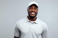 Happy African American man in white polo shirt and cap smiling at camera against gray background for business marketing and lifestyle content.