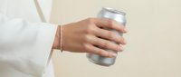Woman hand holding aluminum beverage can against neutral beige background for modern lifestyle and refreshment advertising campaigns.