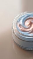 Swirled cosmetic cream with peach and blue tones in clear glass jar on neutral background, suitable for skincare, beauty product packaging, and cosmetics advertising.