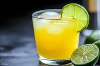 Fresh orange cocktail with lime garnish in glass on dark surface for summer beverage menu and bar advertising.