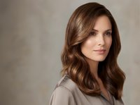 Professional brunette businesswoman with wavy hair in beige blazer against neutral background for corporate marketing and business presentations.