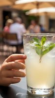Person holding refreshing mojito cocktail with fresh mint leaves and ice at outdoor cafe terrace gathering, summer beverage enjoyment.