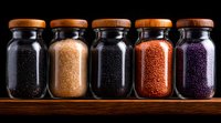 Glass jars with colorful spices and seasonings on wooden shelf against dark background, arranged in row showing variety of textures and natural ingredients.