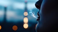 Silhouette profile of woman exhaling smoke against blurred city lights at dusk, creating atmospheric mood with bokeh effect in background.