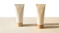 Two minimalist white cosmetic tubes with wooden caps on a beige surface, soft shadows, natural light, eco-friendly skincare packaging concept.