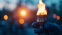 Burning torch flame held in gloved hand against blurred dark background with bokeh lights creates atmospheric evening ambiance for outdoor adventure concepts.