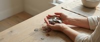 Hands of adult woman in beige sweater counting coins on wooden table, financial planning and budgeting concept for money management designs.
