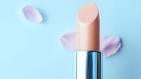 Nude beige lipstick with scattered pink rose petals on soft blue background, minimalist cosmetic product photography for beauty and makeup advertising.