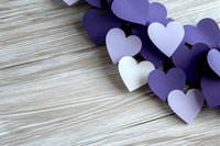Purple and white paper hearts scattered on rustic wooden background, creating romantic composition with soft shadows and copy space for Valentine's day designs.