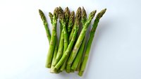 Fresh green asparagus spears arranged in row on white background, isolated healthy vegetable for food and cooking projects, clean professional studio lighting.
