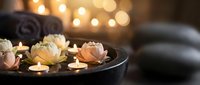 Spa wellness setup with floating lotus candles in dark bowl, towels and warm bokeh lights creating relaxing massage therapy atmosphere for meditation retreat.