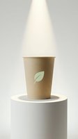 Kraft paper cup with green leaf logo on white cylindrical pedestal under spotlight, eco-friendly beverage packaging for cafes and restaurants.
