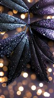 Dark purple leaves covered in water droplets against blurred golden bokeh lights create magical nature macro photography effect for artistic backgrounds.