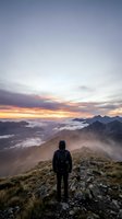 Hiker in black backpack standing on mountain ridge at sunrise overlooking sea of clouds and distant peaks, adventure and exploration concept for travel and outdoor lifestyle.