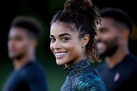 Young African American woman smiling during outdoor fitness training session with diverse group of athletes in background for sports marketing.