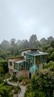 Modern eco-friendly house with green glass panels nestled in lush tropical rainforest canopy on misty overcast day for sustainable architecture concepts.