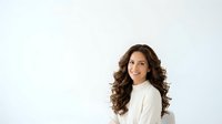 Woman with long wavy brown hair wearing cream-colored sweater against white background, suitable for portrait, business, and lifestyle design projects.