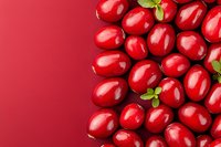 Fresh ripe cranberries with green leaves arranged on red background, top view. Natural healthy berries pattern for seasonal food design and decoration.