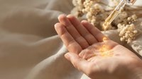 Golden serum drops from glass dropper into cupped female hands with warm sunlight creating natural skincare and wellness moment for beauty routine.