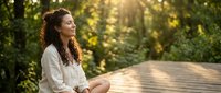 Young mixed-race woman meditating peacefully on wooden deck in sunlit forest. Serene mindfulness practice outdoors with golden hour lighting and natural bokeh.