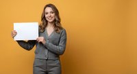 Young professional businesswoman holding blank white paper sign against orange background for marketing presentations and advertising campaigns.