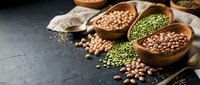 Assorted legumes and pulses in wooden bowls on dark surface with scattered beans and peas for cooking and nutrition.