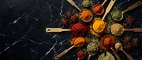Colorful spices and herbs in wooden spoons arranged on dark marble surface. Culinary ingredients for cooking and seasoning food preparation in kitchen.
