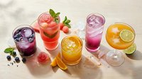 Colorful summer cocktails and mocktails with fresh fruits, ice cubes and mint garnish arranged on light background for refreshing beverage concepts.