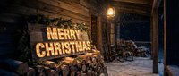 Rustic wooden porch with glowing Merry Christmas marquee sign, stacked firewood, lantern light, and falling snow in a cozy winter cabin setting.