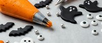 Halloween craft supplies with black paper ghosts, googly eyes and orange glue pen on white surface for spooky DIY projects and seasonal decorations.
